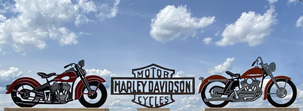 A vintage motorcycle photograph of two Harley Davidsons sitting on a railing.